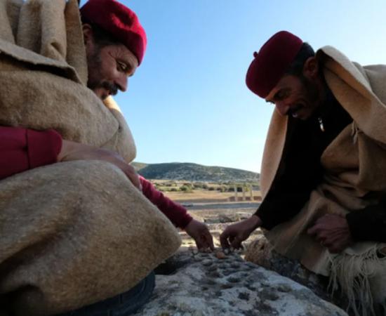 Residents of Tolmeita, dressed in traditional costumes, play a game on the walls within the Cistern Square in Ptolemais