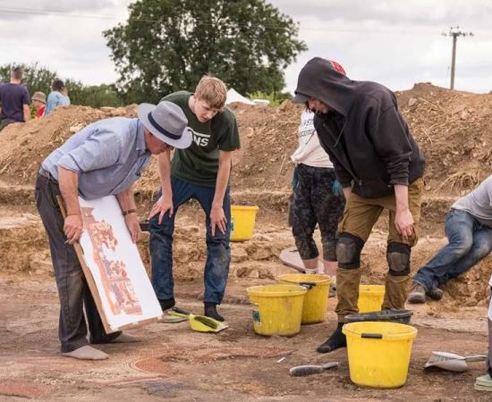 Dr. David Neal making notes on his illustration during the excavation of the Roman mosaic with students from ULAS / University of Leicester. Source: Historic England