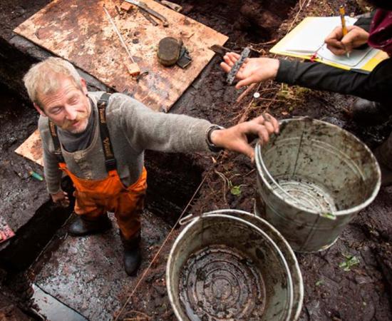 Archaeologist John Maxwell passes up an artifact from the excavation site on Triquet Island. Some of the artifacts were dated to over 14,000 years ago, making it one of the oldest ever sites found in North America. Photo: Grant Callegari/Hakai Institute.