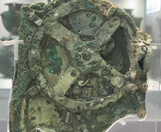 Corroded green bronze fragment with a large four-spoked gearwheel