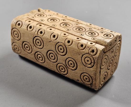Small carved bone box with a sliding lid, decorated with rows of ring and dot circles