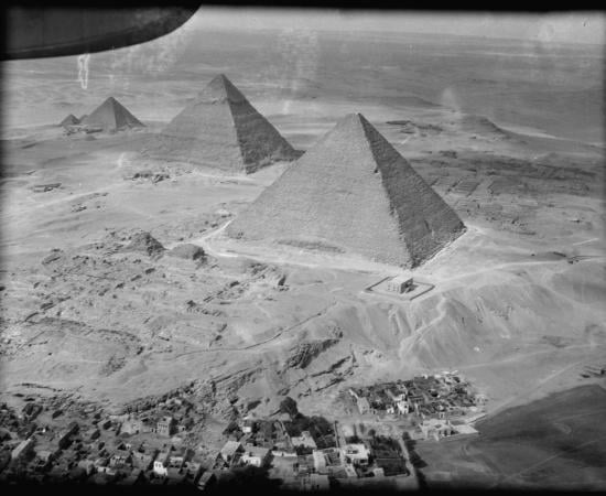 Black and white aerial photograph of the three Giza pyramids in a diagonal line above a village
