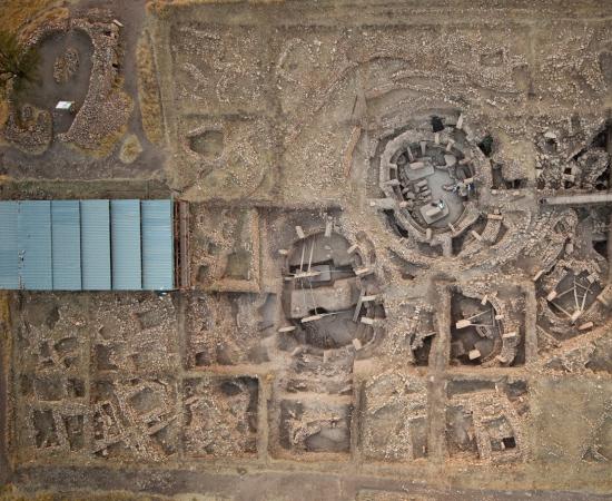 Aerial view of the main excavation area at Göbekli Tepe, with large round stone enclosures ringed by T-shaped pillars and smaller rectangular buildings beside them