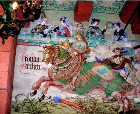 A neo-Gothic mural by Léo Scnug in a French castle depicting a medieval knight about to joust and four women in the audience, painted in the 1910s.
