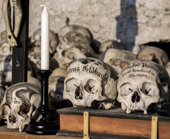 Skulls painted with names, colorful flowers, and crosses in the Charnel House in Hallstatt, Austria. Source: J. Ossorio Castillo / Adobe.