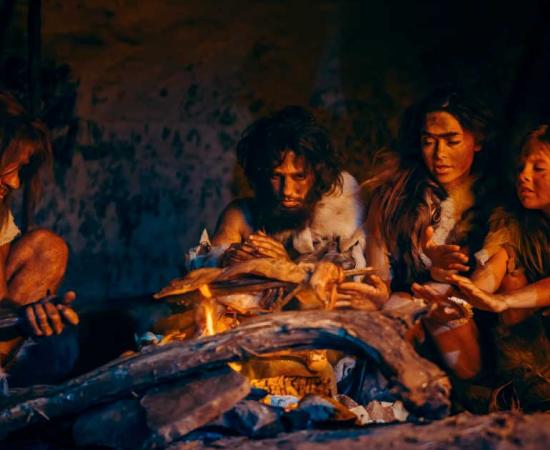 Neanderthal or Homo Sapiens family cooking animal meat over a fire.	Source: Gorodenkoff/Adobe Stock
