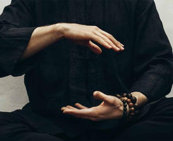 A man in black shirt sitting and doing qigong with his hands directing his body's life energy or qi.        Source: Anna / Adobe Stock