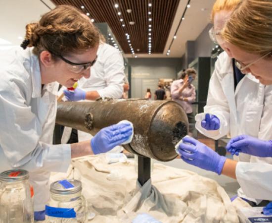 Nautical Archaeology Program graduate students Kimberly Breyfogle ’23 (left), Alyssa Carpenter ’22 (center) and Marissa Agerton ’25 (right) gently clean the exterior of a four-pound bronze cannon used in the Battle of the Alamo.