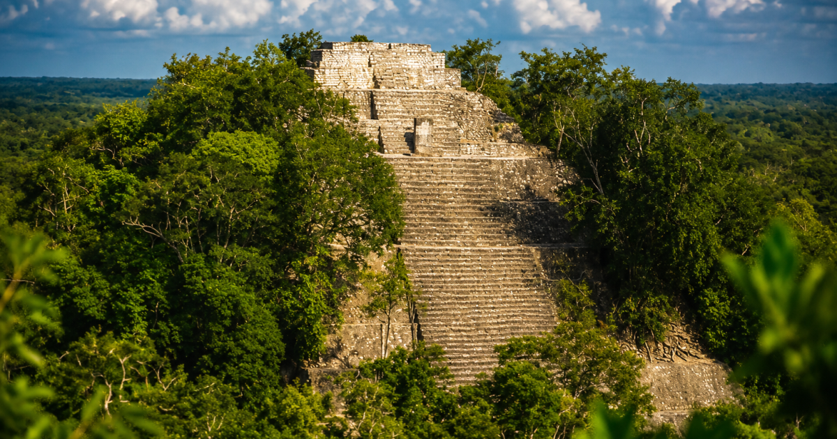 Aerial shot of Calakmul-style jungle ruins with visible structure. Calakmul pyramid rising above the jungle canopy in Campeche, Mexico.