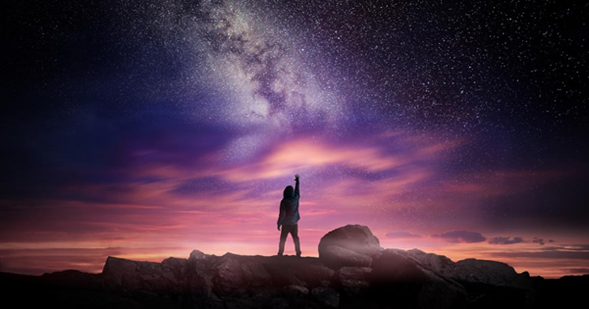 Man standing in a high place reaching up in wonder to the galaxy.