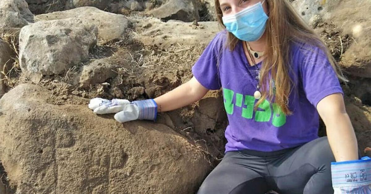 The image shows Ofri Eitan of the Kfar Hanasi pre-military Academi next to a large engraved stone discovered at the Golan Heights fort.             Source: Tidhar Moav / Israel Antiquities Authority