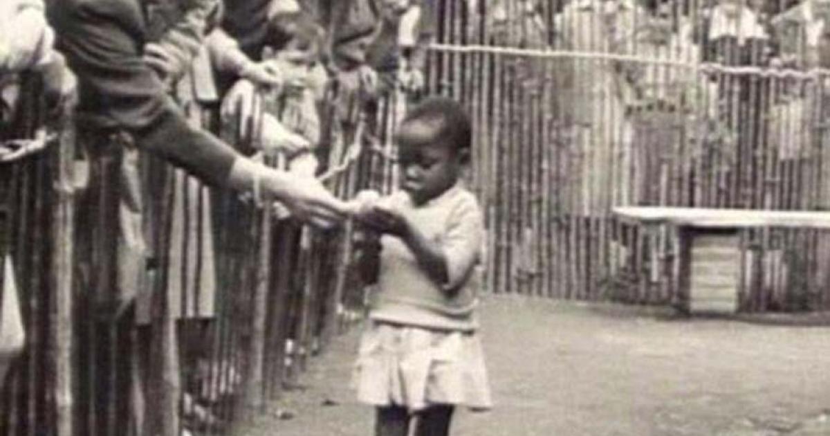 An African girl is shown at the 1958 Expo in Brussels, Belgium that featured a 'Congo Village' with visitors watching her from behind wooden fences