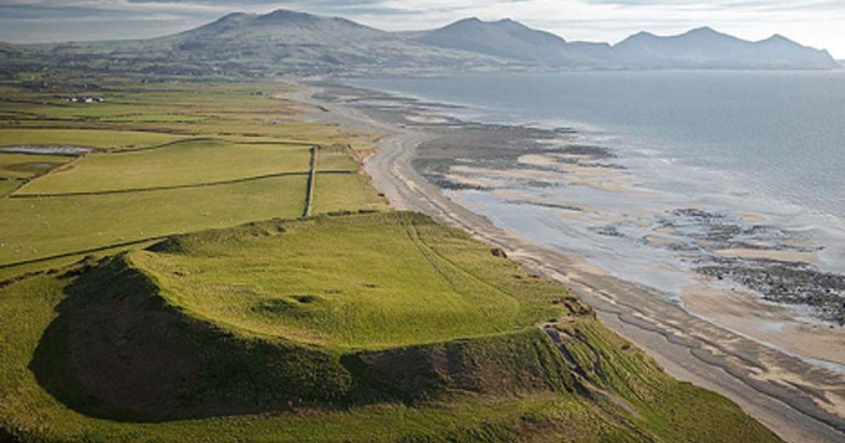 An aerial photograph of Dinas Dinlle Iron Age Hill Fort from the north (suffering from coastal erosion); Gwynedd, Cymru / Wales. Cromlechs & Ancient Sites. (CADW/Visit Wales/CC BY SA 3.0)