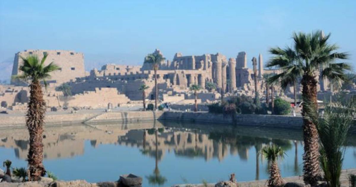 Karnak Temple Complex in Luxor, Egypt, showing the magnificent columns and sacred lake reflecting the ancient structures under clear blue skies.