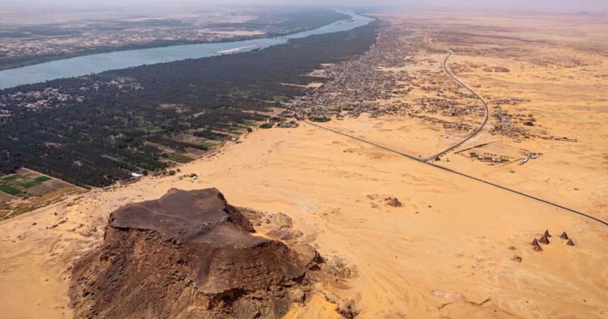 Jebel Barkal (ancient Napata), a UNESCO World Heritage site in northern Sudan, with the sandstone outcrop, temples, and pyramids in the foreground and the Nile and its floodplain in the background, viewed toward the southwest 