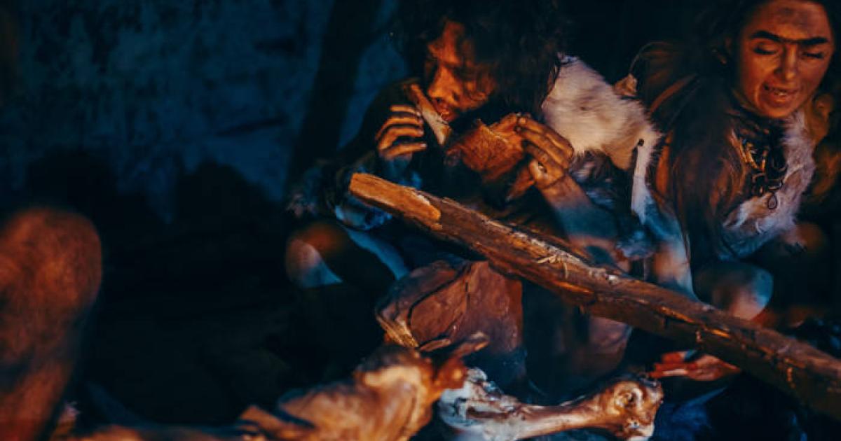 Neanderthal cannibals eating a meat feast by a fire.