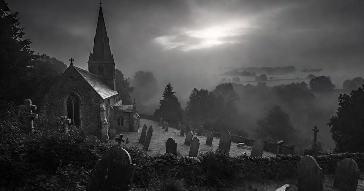 The ancient stone church of Pluckley stands dramatically in a foggy black-and-white landscape,
