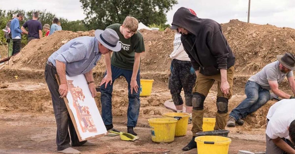 Dr. David Neal making notes on his illustration during the excavation of the Roman mosaic with students from ULAS / University of Leicester. Source: Historic England