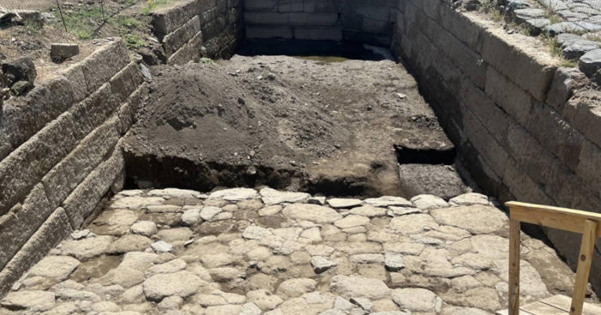 Ancient Roman water basin excavation at Gabii showing stone-lined structure carved into bedrock.