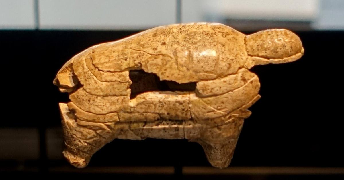 A small mammoth figure carved from mammoth ivory, shown on a museum stand