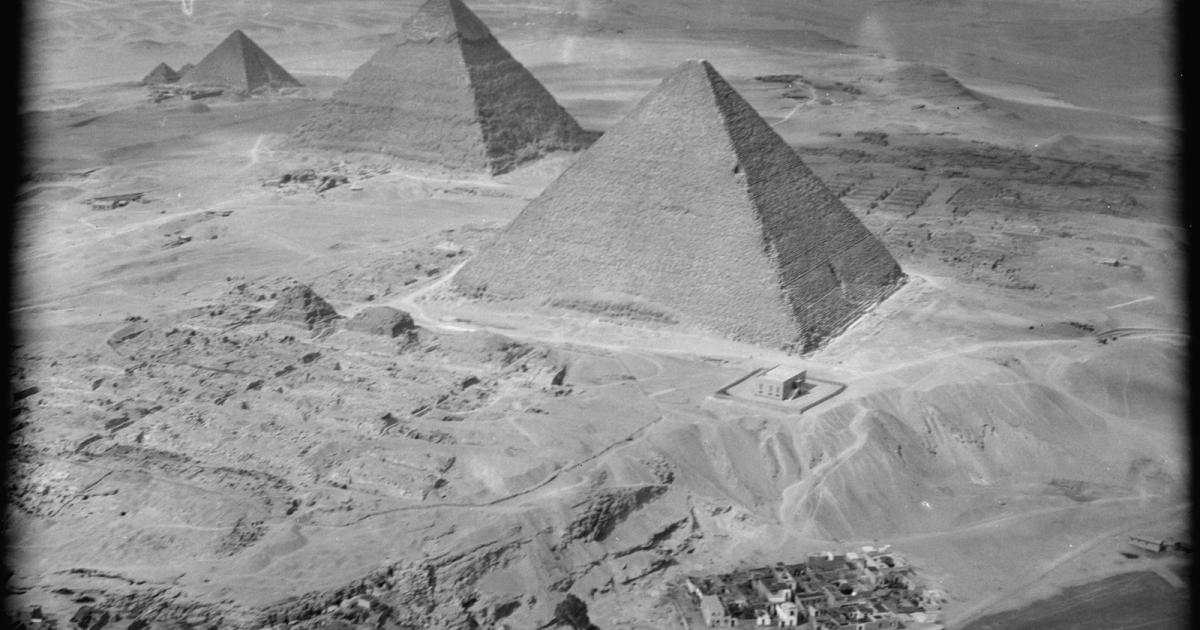 Black and white aerial photograph of the three Giza pyramids in a diagonal line above a village
