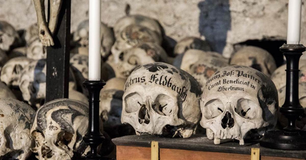 Skulls painted with names, colorful flowers, and crosses in the Charnel House in Hallstatt, Austria. Source: J. Ossorio Castillo / Adobe.