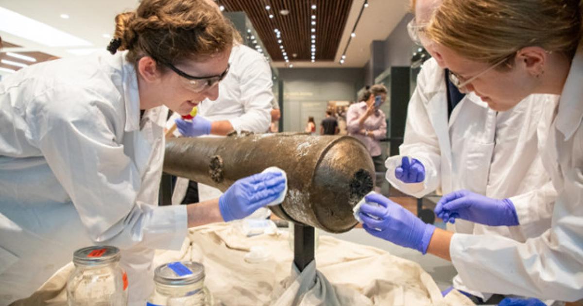 Nautical Archaeology Program graduate students Kimberly Breyfogle ’23 (left), Alyssa Carpenter ’22 (center) and Marissa Agerton ’25 (right) gently clean the exterior of a four-pound bronze cannon used in the Battle of the Alamo.