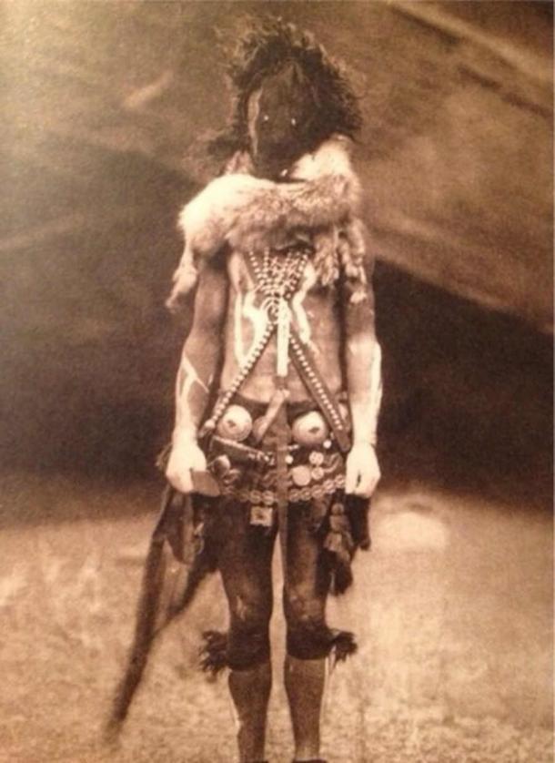 A Navajo man wearing a ceremonial mask and dress of Naayééʼ Neizghání, taken by Edward S. Curtis (c. 1904) (Public Domain)