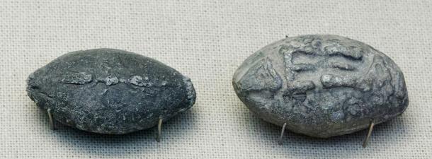 Ancient Greek sling bullets with engravings. One side depicts a winged thunderbolt, and the other, the Greek inscription “take that” in high relief.