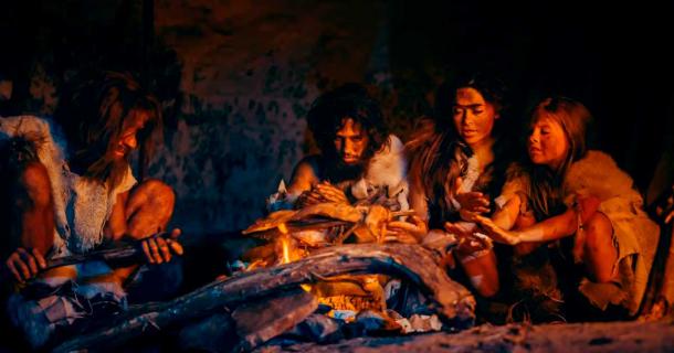 Antigua familia humana cocinando carne animal sobre un fuego. (Gorodenkoff/Adobe Stock)