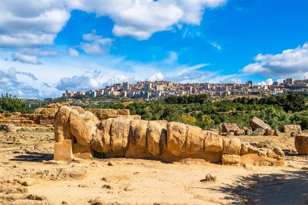 The statue of Atlas lying down with the modern Italian city of Agrigento in the background. (javarman / Adobe Stock)