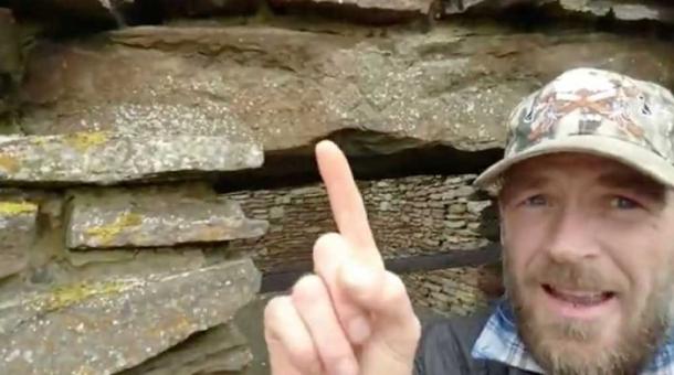 Author at Old Wick Castle in Caithness pointing to a swastika. 07/18/18. (Image: Courtesy of Ashley Cowie)
