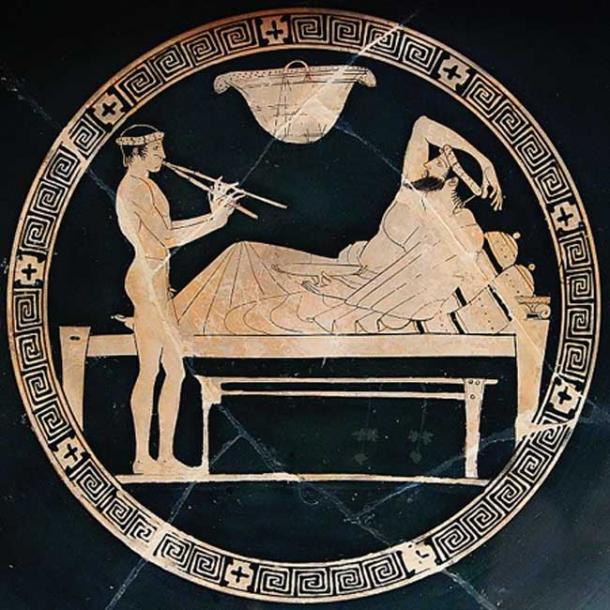 Banquet scene: man reclining on a bench and youth playing the aulos. Tondo of an Attic red-figure cup