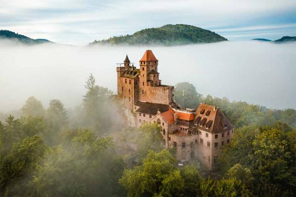 Zámok Burg Berwartstein je realistický fantasy hrad ukrytý vo Falckom lese v juhozápadnom Nemecku.  Táto skalná pevnosť, ktorá sa prvýkrát spomína v roku 1152, bola postavená na obranu Falcka v stredoveku a niektoré miestnosti, schodiská a chodby sú vytesané do skaly.  (Vincent / Adobe Stock)