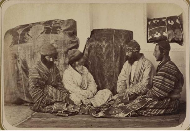 Four Jewish men seated on the ground next to two large covered bundles, inspecting the dowry.
