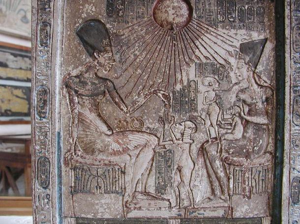 Stele: Akhenaton si siede su uno sgabello sul lato sinistro, consegnando un gioiello di sua figlia maggiore (e forse balia di Tut) Meritaten, che sta di fronte a lui.  A destra gioca con due delle loro figlie in grembo, Maketaton e Ankhesenpaaten.