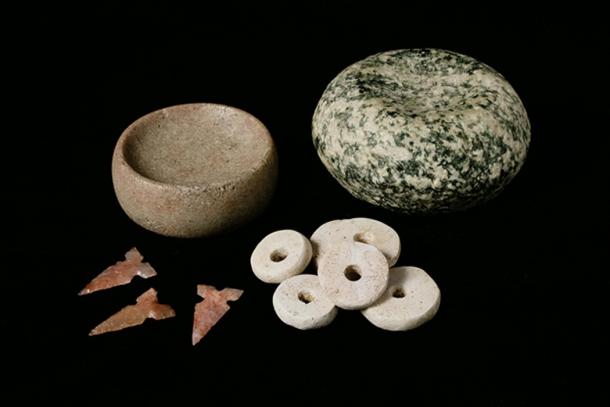 Mound 72 at Cahokia held several mass graves but also burials of high-status individuals, some of which included items like these artifacts. Pictured here are chunky stones likely used in games, Cahokia-style tri-notched projectile points, and marine shell disc beads like those used in the beaded burial at Cahokia.