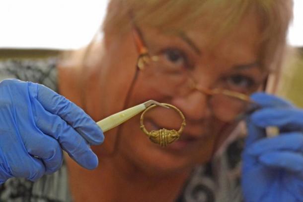 Professor Bonnie Petrunova inspects one of the pieces of jewelry. (Image: National History Museum, Bulgaria)