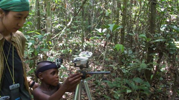 Young Mbendjele boy of age 8.5 years pointing at a food location. Here with researcher Haneul Jang in the tropical rainforest of the Republic of Congo. (© Karline Janmaat)