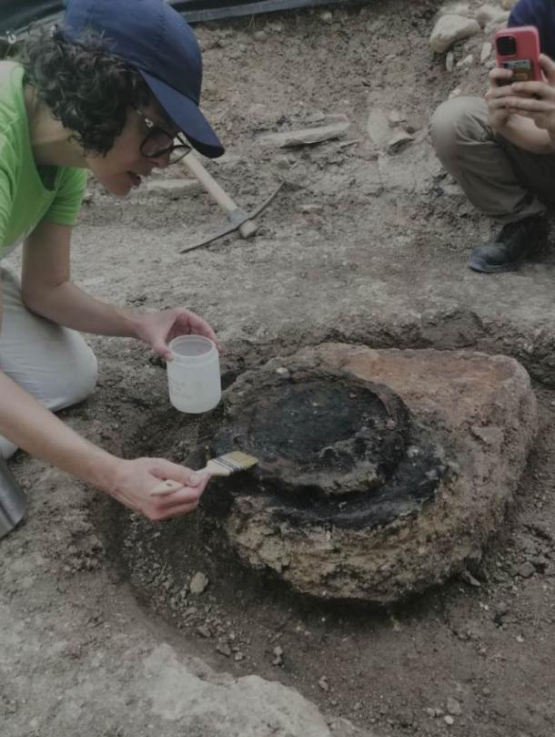 An archaeologist brushing dirt from a buried artifact at the site of the brewery