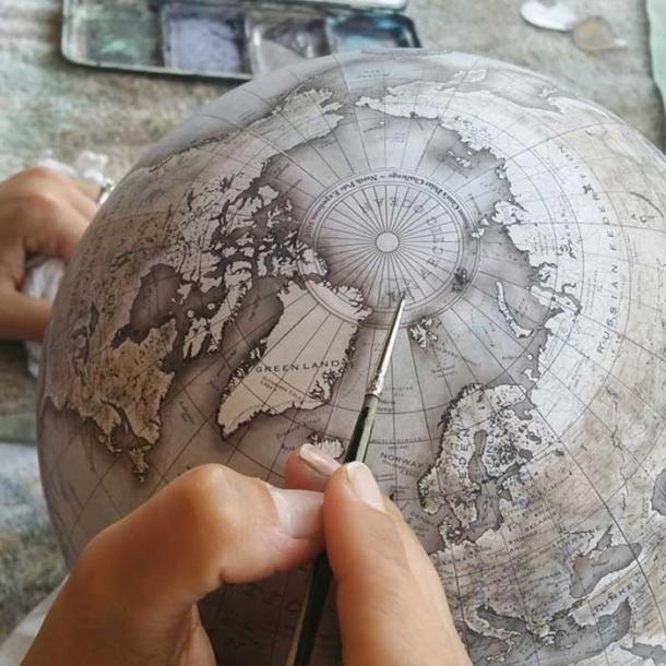 An artist painting details onto a globe.