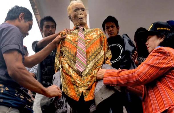 A family dresses up the corpse of a family member in new clothes