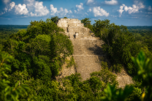 Aerial shot of Calakmul-style jungle ruins with visible structure. Calakmul pyramid rising above the jungle canopy in Campeche, Mexico.