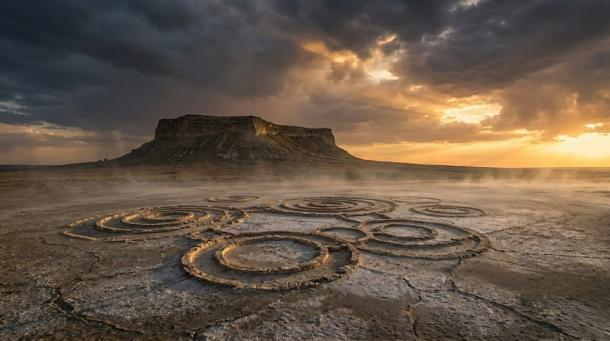 A haunting plateau rises over the cracked, salt-crusted desert. Mysterious circles etched into the ground hint at ancient secrets. Dramatic light and low mist shroud the landscape in enigma.