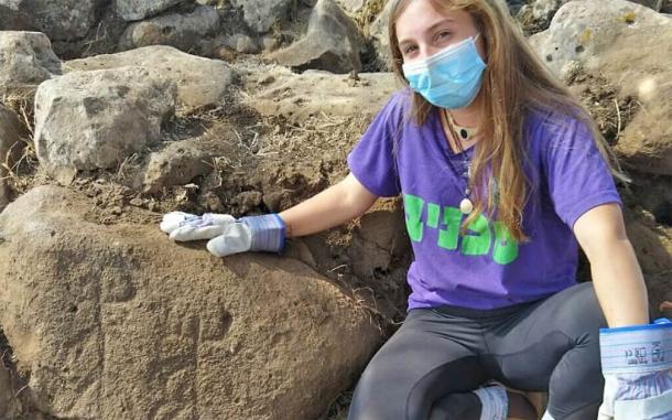 The image shows Ofri Eitan of the Kfar Hanasi pre-military Academi next to a large engraved stone discovered at the Golan Heights fort. Source: Tidhar Moav / Israel Antiquities Authority