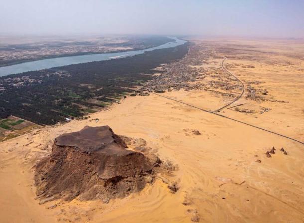 Jebel Barkal (ancient Napata), a UNESCO World Heritage site in northern Sudan, with the sandstone outcrop, temples, and pyramids in the foreground and the Nile and its floodplain in the background, viewed toward the southwest 
