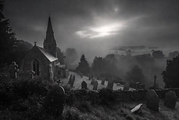 The ancient stone church of Pluckley stands dramatically in a foggy black-and-white landscape,