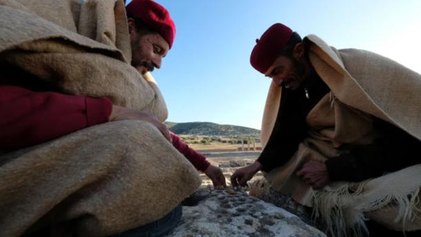 Residents of Tolmeita, dressed in traditional costumes, play a game on the walls within the Cistern Square in Ptolemais