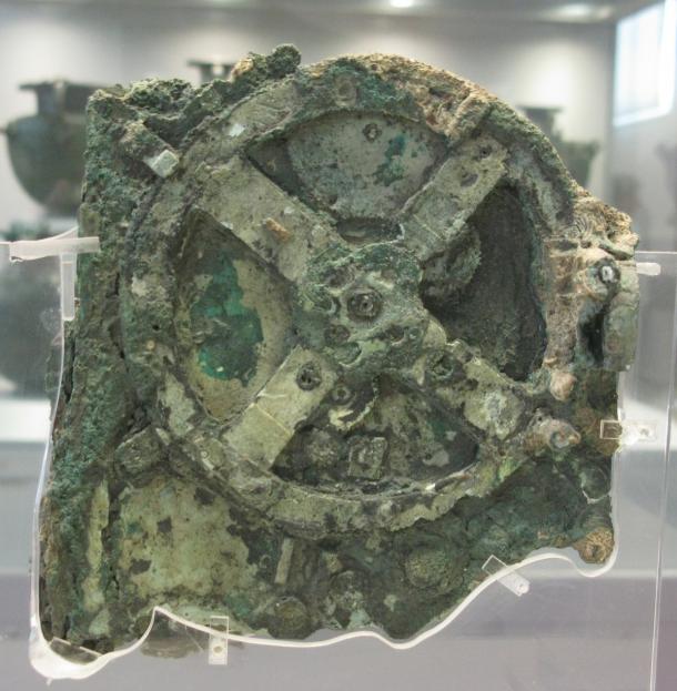 Corroded green bronze fragment with a large four-spoked gearwheel