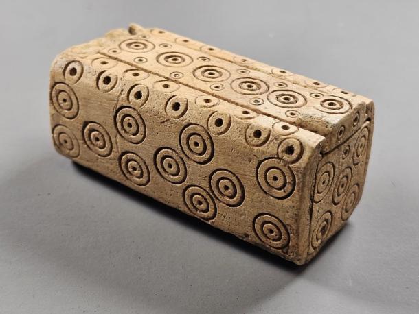 Small carved bone box with a sliding lid, decorated with rows of ring and dot circles